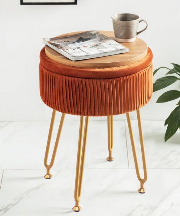 A dark orange velvet ottoman with elegant gold legs.