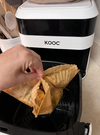 A reviewer pulling the liner and any mess out of the air fryer.