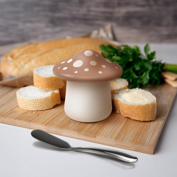 A mushroom-shaped butter keeper resting on a counter beside a slice of buttered bread