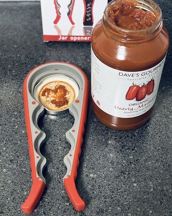 A jar of marinara sauce with the opener next to it on a countertop; the jar is open, highlighting the convenience of kitchen gadgets.