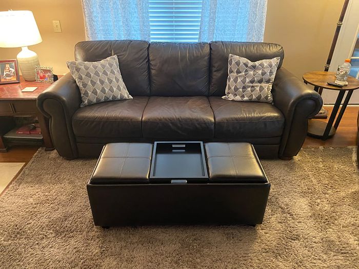 A reviewer's photo of a brown faux leather ottoman with reversible tray cushions