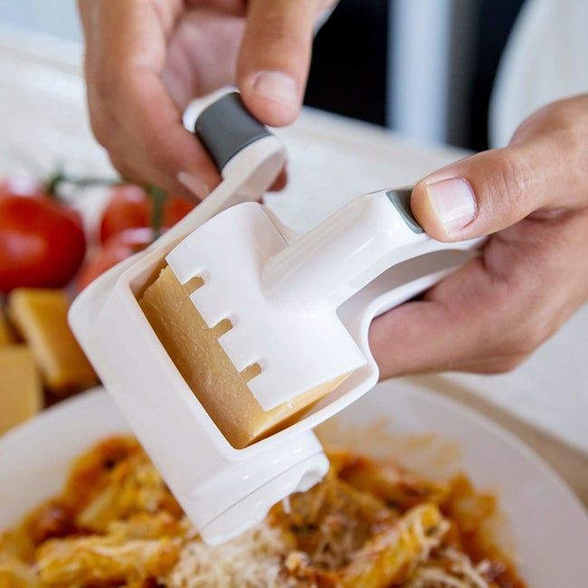 A person grating cheese and sprinkling it over pasta using a grater.