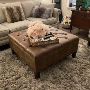 A photo review showing a brown faux leather ottoman with a large square design, resting on four legs.