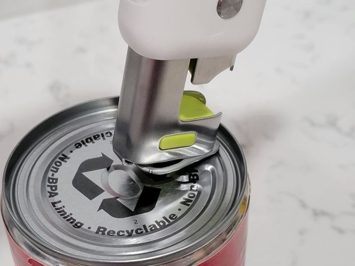 An electric can opener cutting into a can lid, showing a recycling symbol and describing its features.
