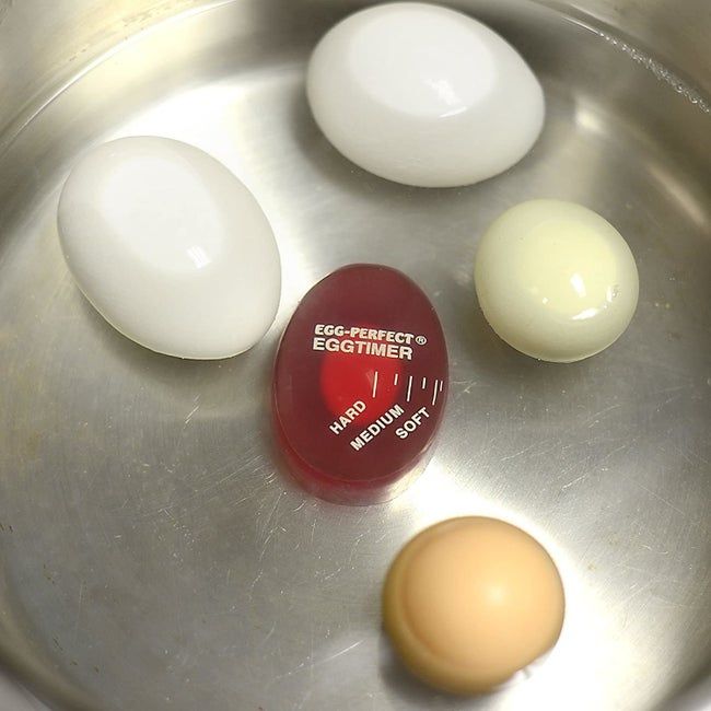 An egg-shaped timer sitting in a pot with eggs.