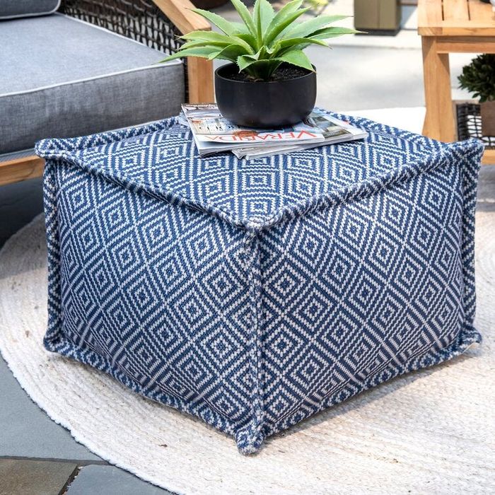 An image of the blue and white square ottoman adorned with magazines and a plant on top.