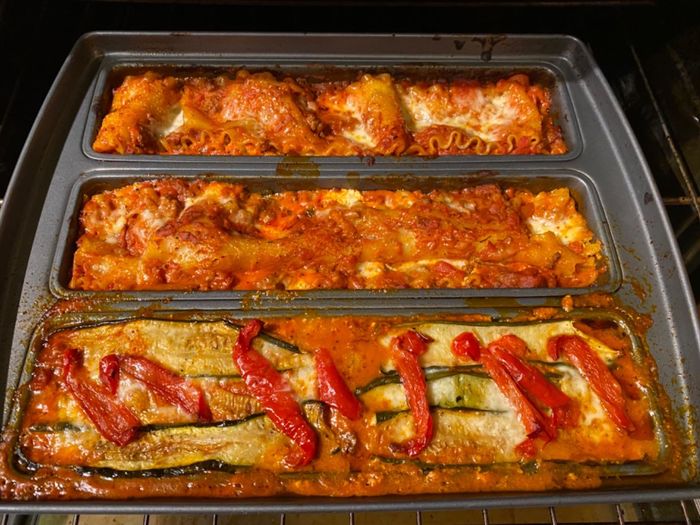 Three trays of lasagna, each adorned with unique toppings, baking in the oven. The golden-brown surface of the lasagna is perfectly crisp and inviting.