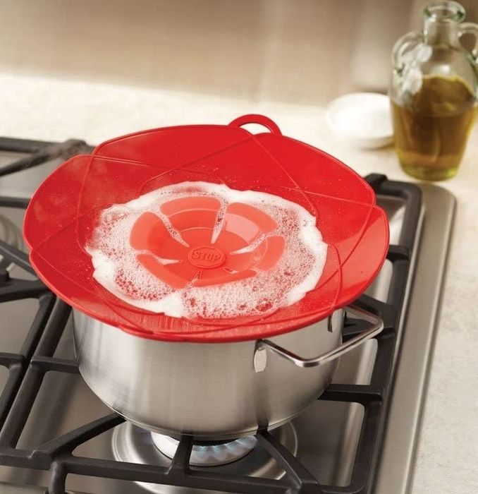 A red spill stopper sits on top of a pot on the stove with boiling water, showing how it effectively prevents the water from spilling over.