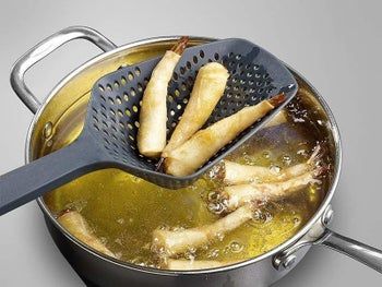 A pot of boiling oil with a colander-like spoon lifting wontons from the oil.