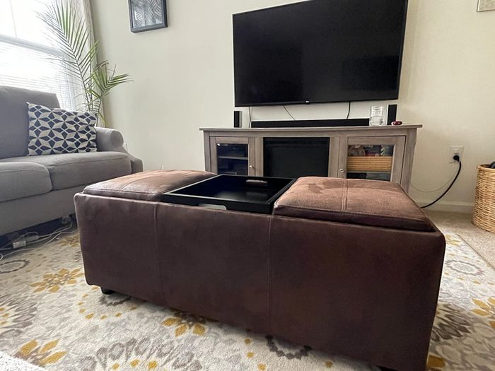 A reviewer's photo of a brown faux leather ottoman with reversible tray cushions