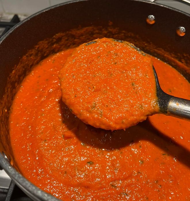 A pot of hearty homemade tomato sauce with a ladle lifting a rich portion of the thick sauce, ideal for pairing with pasta or pizza.