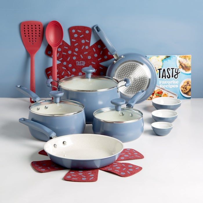 Cookware set with various pots, pans, lids, red utensils, a cookbook, and bowls arranged on a clean white surface