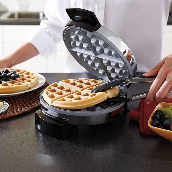 A person making waffles with a waffle maker, pouring batter into the machine