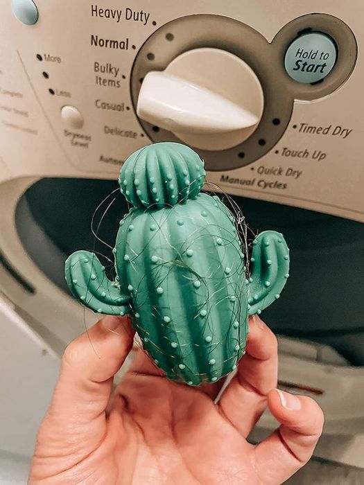 A hand holding green dryer balls, with strands of hair wrapped around them