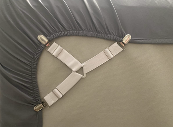 A white, three-way adjustable fastener attached to a fitted sheet to secure it under a mattress