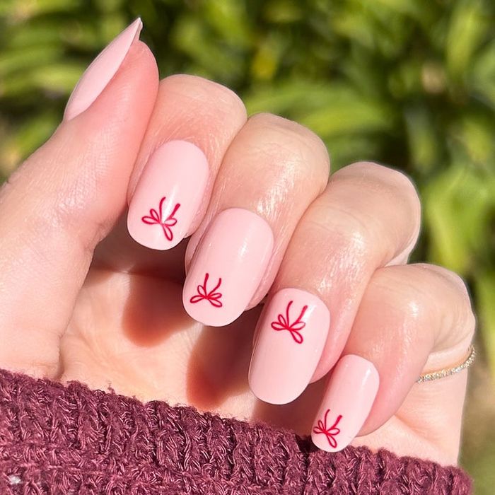 a model showcasing short, oval press-on nails adorned with a stylish bow design