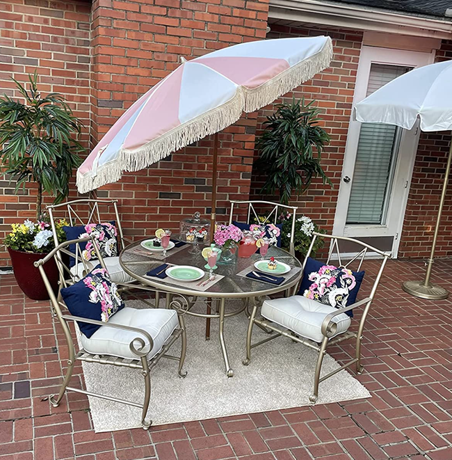 A pink and white striped umbrella with fringe set up on an outdoor table