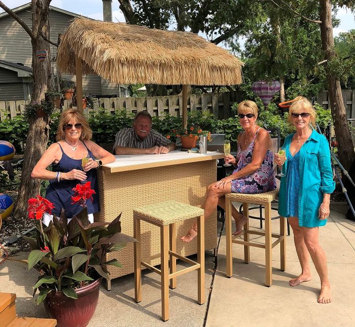 A group of four people enjoying drinks and good company at a tiki bar in a backyard setting.