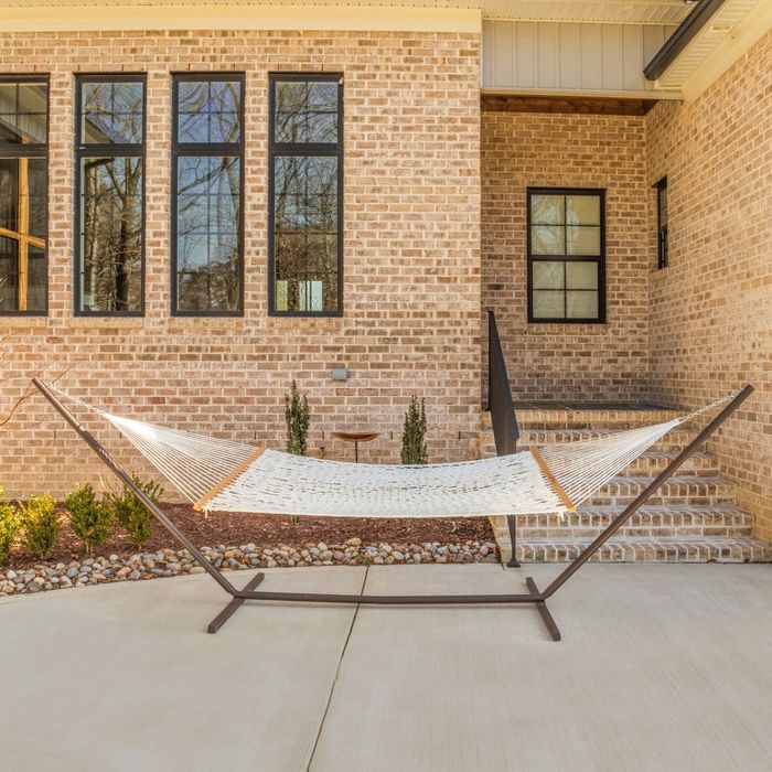 A hammock nestled outside a brick house with large windows and a staircase. Small plants are placed in front of the house for added charm.