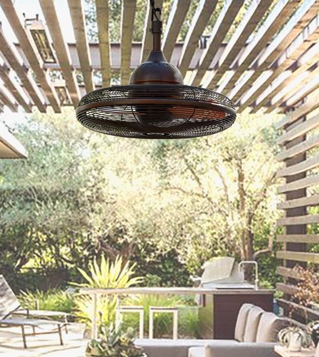 An industrial-style ceiling fan hangs from a pergola in a sunlit outdoor seating area, surrounded by lush greenery in the background.