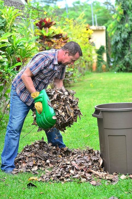 A person demonstrating the leaf scoops, using them to transfer a large handful of leaves into a trash can.