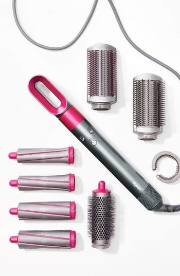 The sleek silver base with a compact oval-shaped hair dryer attached, surrounded by interchangeable heads in grey and pink accents.