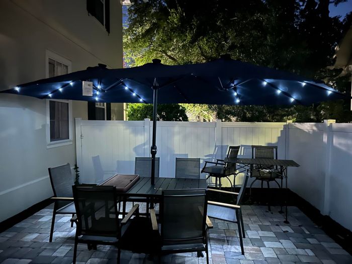 Patio setup featuring a table, chairs, and a large umbrella with integrated LED lights, placed in a backyard with a fence as the backdrop