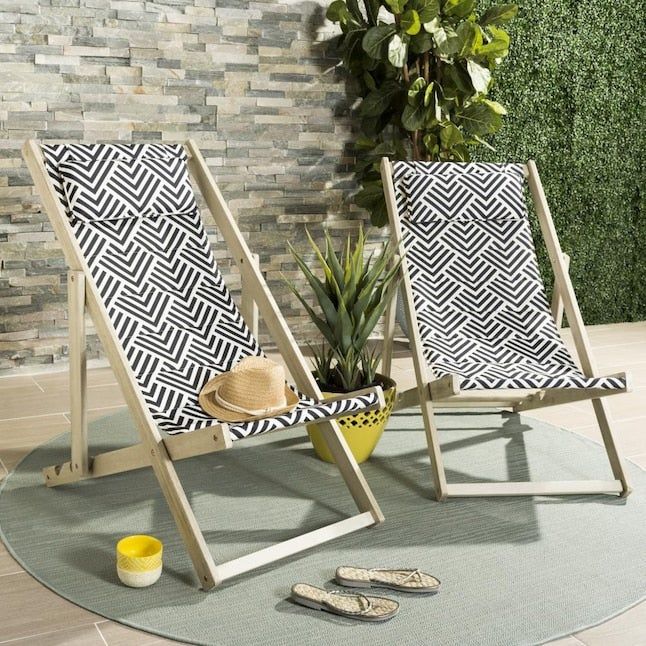 Two deck chairs with patterned fabric placed on a round rug, accompanied by a potted plant. A straw hat rests on one chair, with a pair of sandals and a yellow cup nearby.