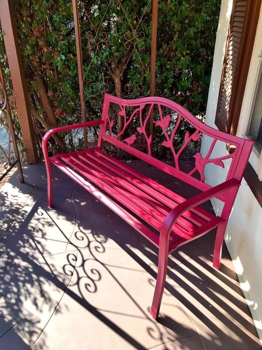 A metal bench featuring a bird and tree design, positioned on a porch casting shadows on the ground