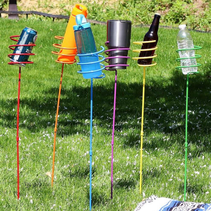 Five garden stakes with spiral holders, each holding a different type of drinkware, placed in a grassy yard