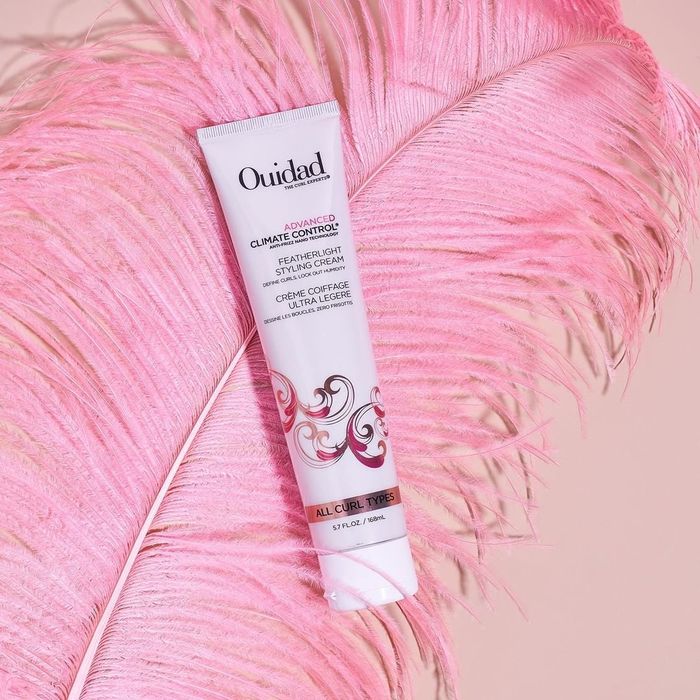 Ouidad Advanced Climate Control Featherlight Styling Cream resting on a pink feather.