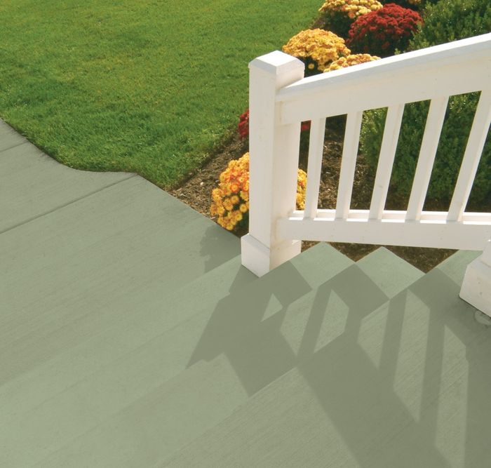 A white railing stands beside green paved steps, with vibrant flowers in the background. Grass and a flowerbed can also be seen. Text: