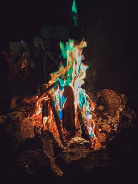 A comforting campfire with vibrant, multicolored flames surrounded by rocks, with empty chairs placed around it.