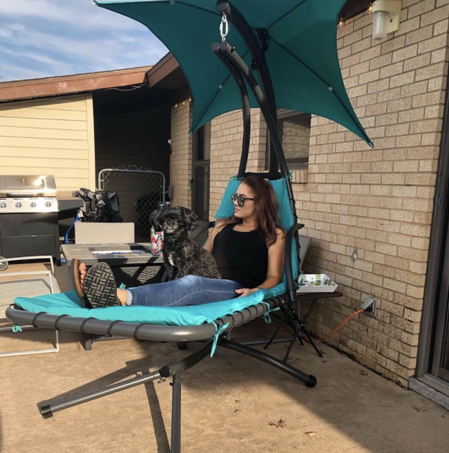 A reviewer relaxing in a suspended chaise lounge chair with an umbrella providing shade.