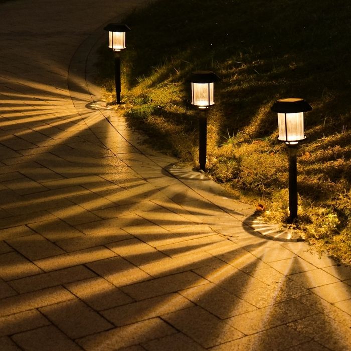 Solar-powered pathway lights create intricate patterns on a brick walkway at night, illuminating the grassy edges.