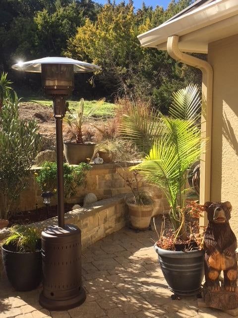 A cozy outdoor patio featuring potted plants, a metal patio heater, and a whimsical wooden bear statue, with a stone retaining wall in the background