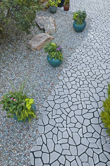 A garden path featuring a cracked pattern winds through a beautifully landscaped area with various potted plants and decorative rock formations.