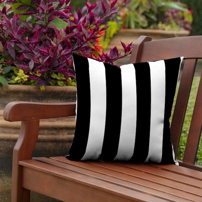 A wooden bench adorned with a black and white striped throw pillow, positioned in front of a lush garden filled with potted plants.