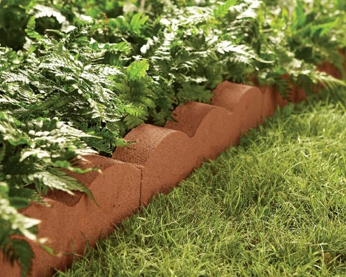A garden scene with a neat border of bricks, featuring ferns on one side and a lush, green lawn on the other.