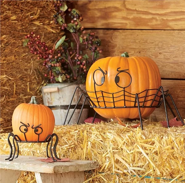 Fierce-looking pumpkins with spider legs, placed on hay and a wooden bench, surrounded by rustic decor with a barrel holding berries and leaves