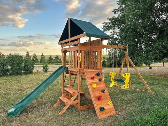 A wooden playset featuring a slide, swings, and a climbing wall, set in an outdoor backyard area, perfect for children's playtime.