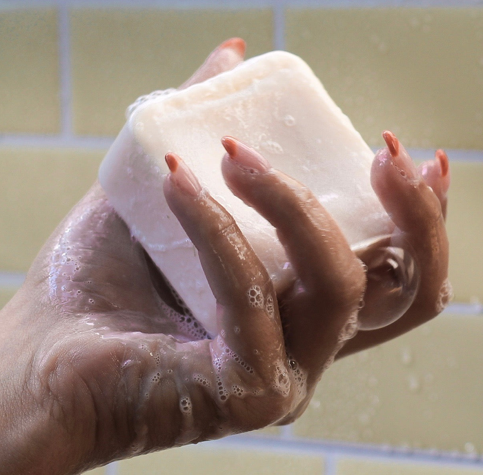 A hand gripping a bubbly square-shaped shampoo bar.