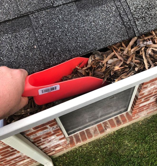 A reviewer using the red scoop to clean out leaves from their gutter.