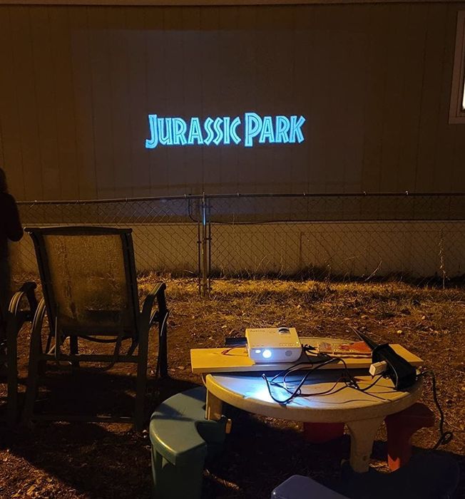 A reviewer’s image showing the projector displaying Jurassic Park on the side of a house