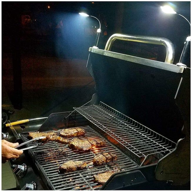 A person grilling meat at night with the barbecue light magnetically attached to the grill.