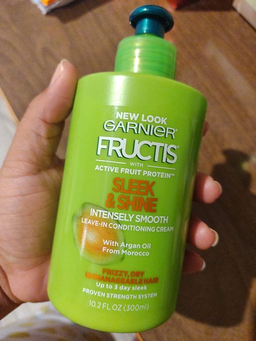 A reviewer captures a photo while holding a bottle of leave-in conditioner.