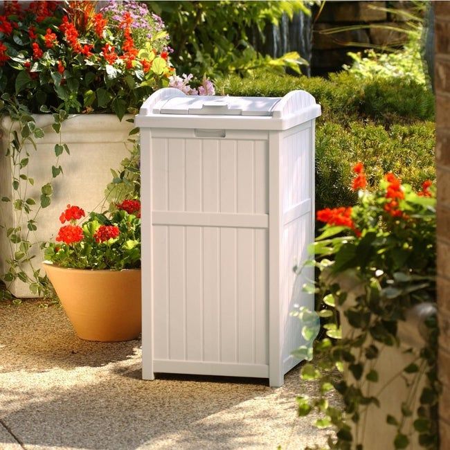A white trash can placed outside next to a garden