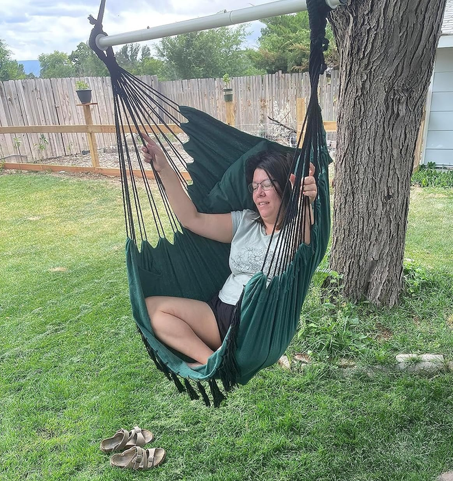 A person lounging in a dark green hammock outdoors