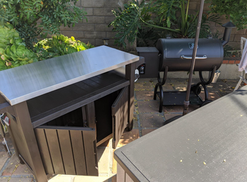 The cart with its cabinet doors wide open, positioned next to a grill.