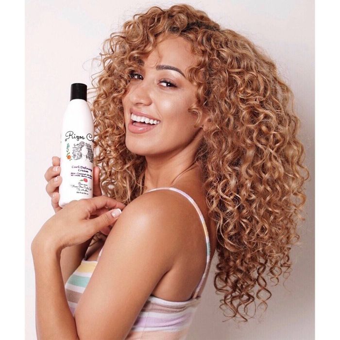 A model with curly hair showcasing the bottle of curl defining cream